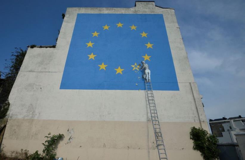 An artwork attributed to street artist Banksy, depicting a workman chipping away at one of the 12 stars on the flag of the European Union, is seen on a wall in the ferry port of Dover, Britain May 7, 2017 (photo credit: REUTERS)