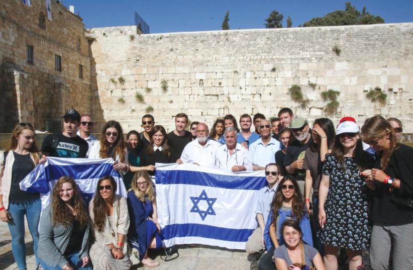 DEPUTY FOREIGN MINISTER Tzipi Hotovely (standing behind left corner of flag) and the three paratroopers from David Rubinger’s iconic 1967 photo (in white shirts) pose with international students at the Western Wall May 11, 2017 (photo credit: MARC ISRAEL SELLEM/THE JERUSALEM POST)