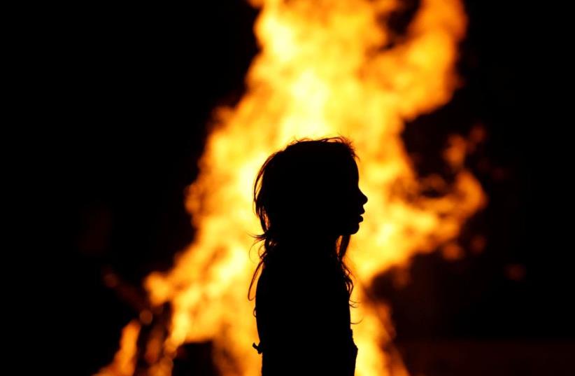 An Ultra-Orthodox Jewish girl stands around a bonfire as she celebrates the Jewish holiday of Lag Ba'Omer in the city of Ashdod, Israel May 13, 2017.  (photo credit: REUTERS)