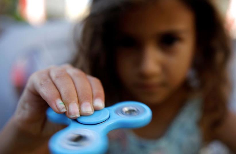 A girl performs tricks using a fidget spinner during a contest held in Ashdod, Israel May 11, 2017 (photo credit: REUTERS)