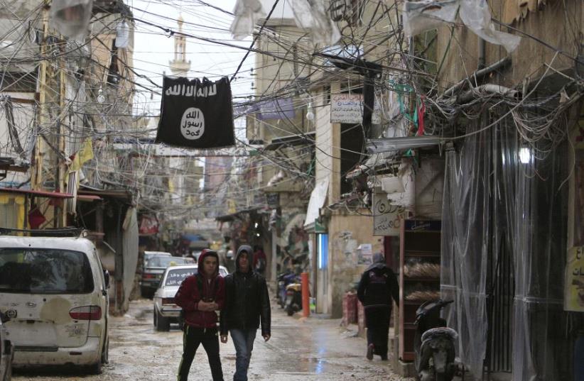 Youth walk under an Islamic State flag in Ain al-Hilweh Palestinian refugee camp, near the port-city of Sidon, southern Lebanon January 19, 2016. (photo credit: ALI HASHISHO/REUTERS)