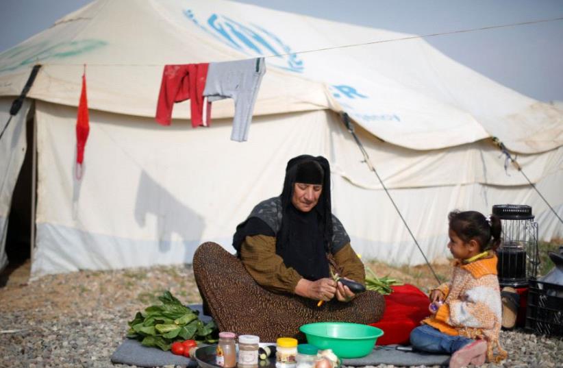 A displaced woman who fled the Islamic State stronghold of Mosul with her family makes the food in front of her tent at Hassan Sham camp, east of Mosul, Iraq (photo credit: MUHAMMAD HAMED / REUTERS)