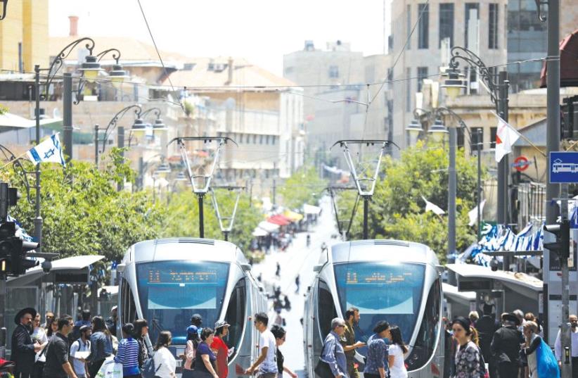 Pedestrians cross a street next to the light rail trams in Jerusalem in May (photo credit: REUTERS)