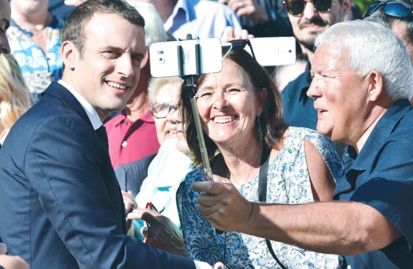 FRENCH PRESIDENT Emmanuel Macron (left) poses for a selfie after voting in the second round of parliamentary elections   (photo credit: REUTERS)