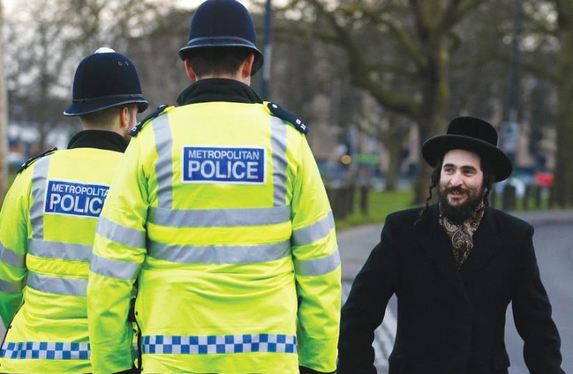 A MEMBER of the Jewish community walks in north London in 2015 as police officials stand watch. (photo credit: REUTERS)