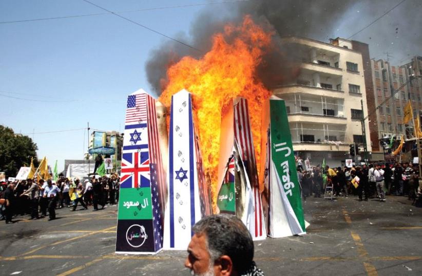 Iranian demonstrators burn a structure displaying the flags of the US, Britain, and Israel during a rally marking al-Quds (Jerusalem) Day in Tehran in 2015; the green banner reads ‘Saud family’ (photo credit: REUTERS)