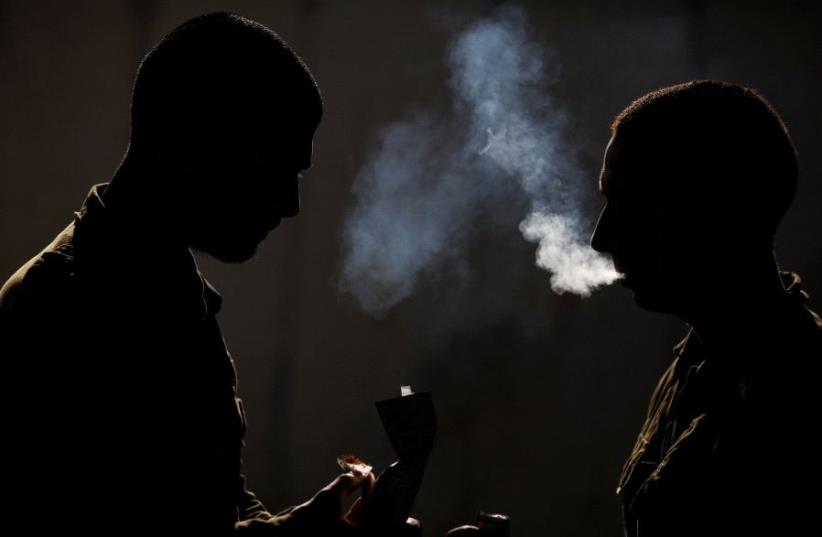 Silhouetted Israeli soldiers from the Home Front Command Unit take a smoking break during an urban warfare drill inside a mock village at Tze'elim army base in Israel's Negev Desert June 11, 2017 (photo credit: REUTERS/AMIR COHEN)