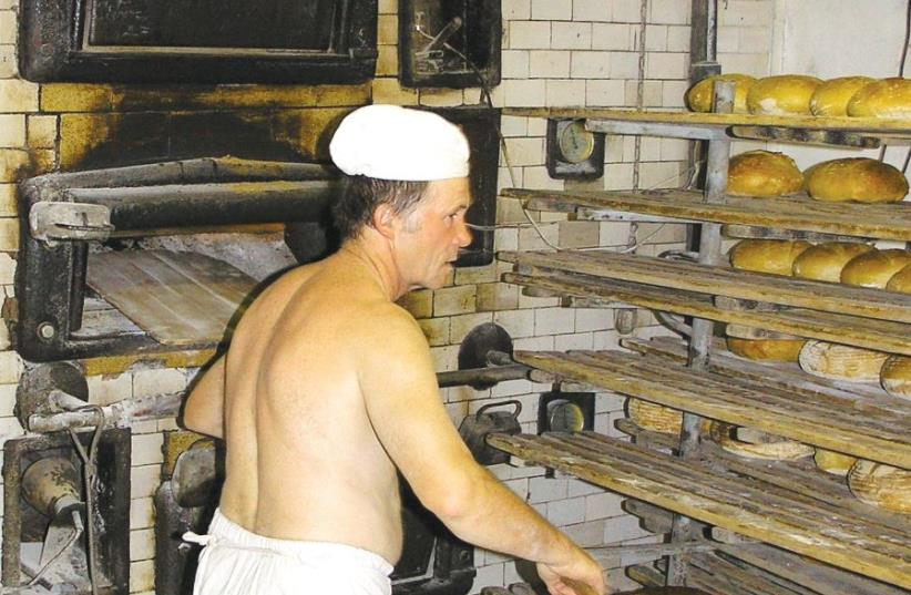 A traditional baker in Poland removes fresh bread from the oven (photo credit: Wikimedia Commons)