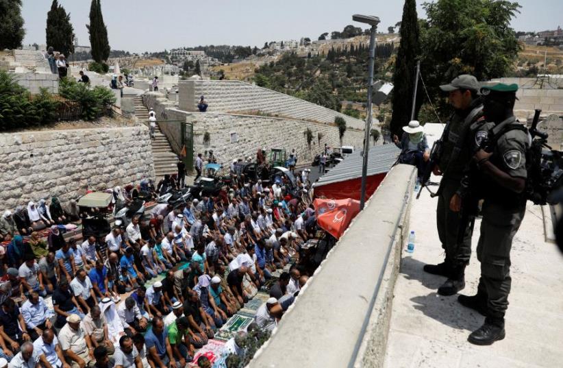 Israeli border police officers stand guard as Palestinians pray at Lions' Gate, the entrance to Jerusalem's Old City, in protest over Israel's new security measures at the Temple Mount July 20, 2017. (photo credit: REUTERS)