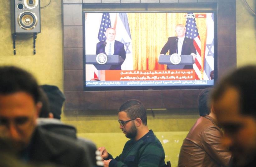 PALESTINIANS GATHER in a coffee ship in Hebron, where a TV screen shows US President Donald Trump and Prime Minister Benjamin Netanyahu participating in a joint press conference in February. (photo credit: REUTERS)