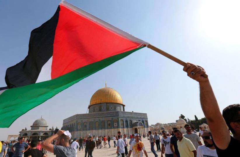 The Dome of the Rock is seen in the background as a man waves a Palestinian flag upon entering the Temple Mount, after Israel removed all security measures it had installed at the compound, in Jerusalem's Old City July 27, 2017. (photo credit: REUTERS)