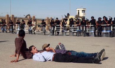 Protesters lie down near security forces in front of the court house where Mubarak will stand trial