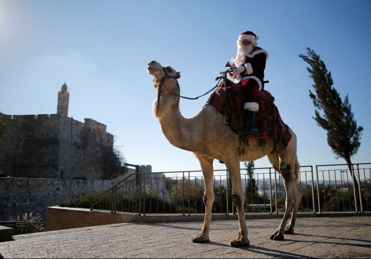 Israeli-Arab Issa Kassissieh wears a Santa Claus costume as he rides a camel during an annual Christmas tree distribution by the Jerusalem municipality, December 20, 2016. (Reuters)