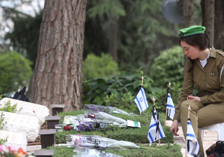 An IDF soldier seats next to a gravestone at the national military cemetery on Mount Herzl in Jerusalem on Memorial Day, May 1, 2017 (MARC ISRAEL SELLEM)‏