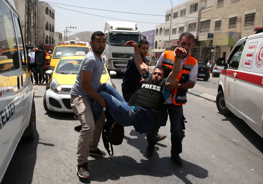 A wounded Palestinian reporter is carried by a medic and civilians on May 18, 2017 near the Hawara military checkpoint. (JAAFAR ASHTIYEH / AFP)