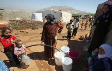 Syrian refugees fill buckets with water.