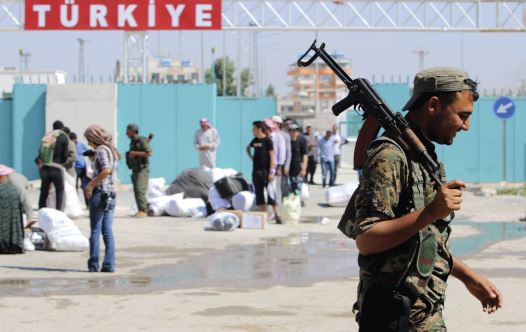 A KURDISH People&rsquo;s Protection Units (YPG) fighter walks near residents who had fled Tel Abyad, as they reenter Syria from Turkey