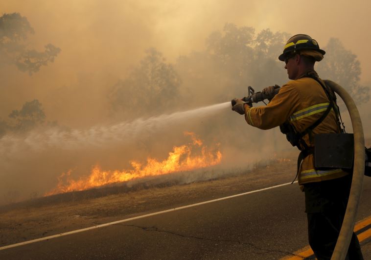 A firefighter uses a hose to extinguish flames. (credit: REUTERS)