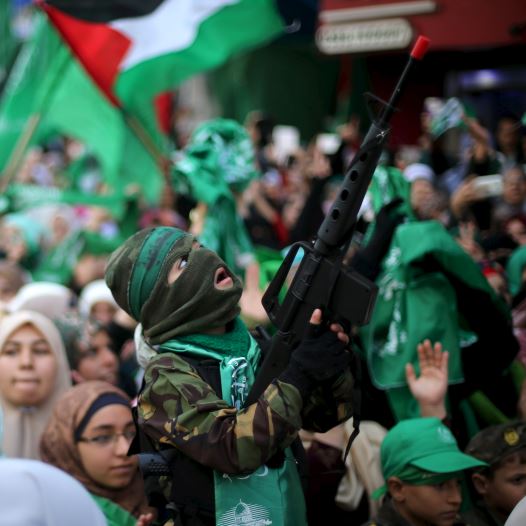A masked Palestinian boy holds a toy gun as he takes part in a rally marking the 28th anniversary of Hamas' founding