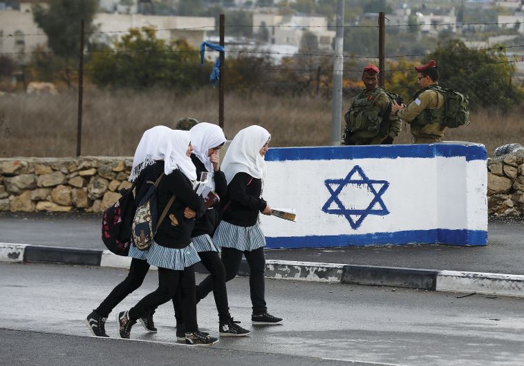 PALESTINIAN SCHOOL girls walk past Israeli soldiers at a checkpoint at a entrance to the village of Beit Einun near Hebron (credit: REUTERS)