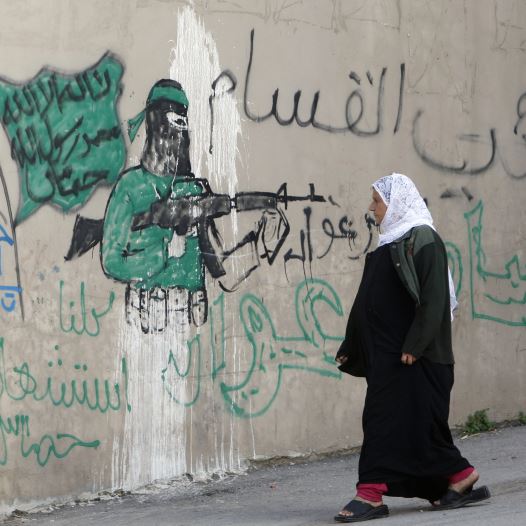 A Palestinian woman walks past a wall with graffiti depicting a gunman from the Al-Qassam brigades, the armed wing of the Hamas movement, in the West Bank village of Awarta.  The graffiti reads ''All of us are martyrs.'' (credit: ABED OMAR QUSINI/REUTERS)