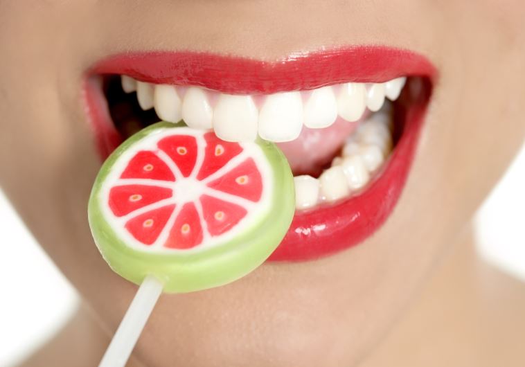 A woman with perfect teeth chews on a lollipop (credit: INGIMAGE)