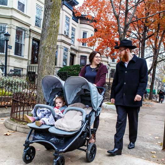 Chabad-Lubavitch Rabbi Mendel Alperowitz, right, Mussie Alperowitz, left, and their two daughters, ages 18 months and 2 months, walk in Crown Heights, Brooklyn. (credit: ELIYAHU PARYPA / CHABAD.ORG)