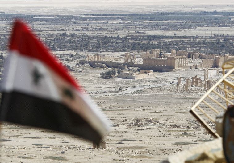 A Syrian national flag flutters as the ruins of the historic city of Palmyra are seen in the background, in Homs Governorate, Syria April 1, 2016.