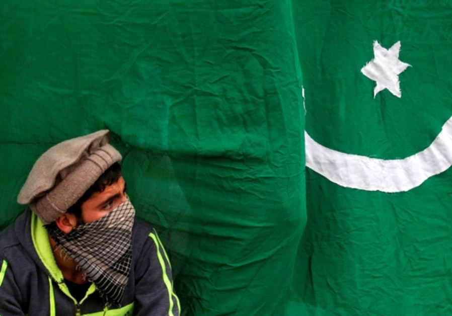 A masked protester sits next to a flag of Pakistan during an anti-Indian protest  (credit: REUTERS)