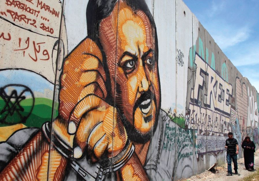 PALESTINIANS WALK past graffiti depicting jailed Fatah leader Marwan Barghouti, currently serving five life terms for terrorism, on a section of the security wall on the road to Ramallah. (credit: REUTERS)