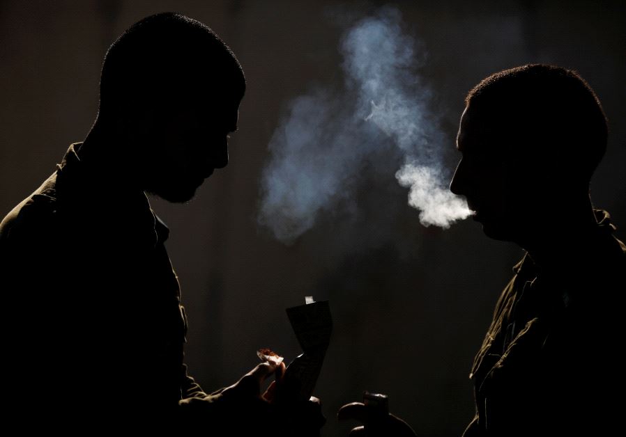 Silhouetted Israeli soldiers from the Home Front Command Unit take a smoking break during an urban warfare drill inside a mock village at Tze'elim army base in Israel's Negev Desert June 11, 2017 (credit: REUTERS/AMIR COHEN)