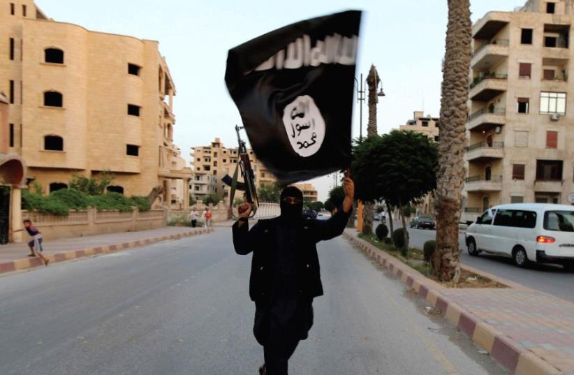 A MEMBER of ISIS waves the group’s flag in Raqqa (photo credit: REUTERS)