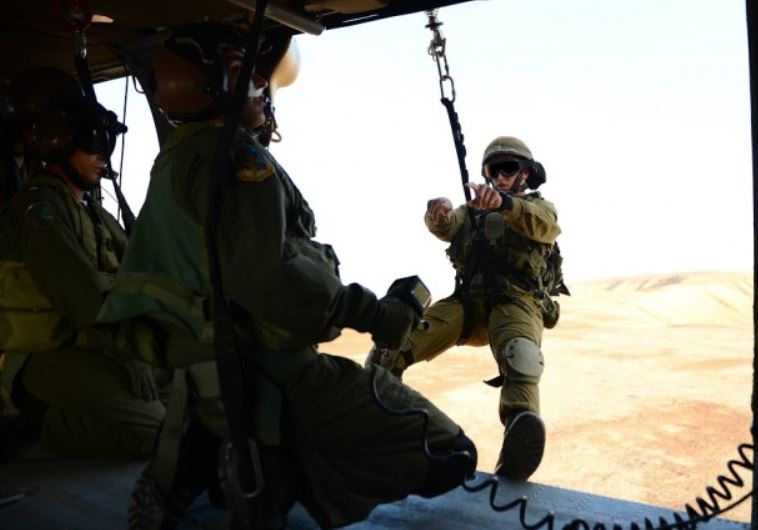 A crew chief directs an IDF soldier attached to the helicopter by a harness