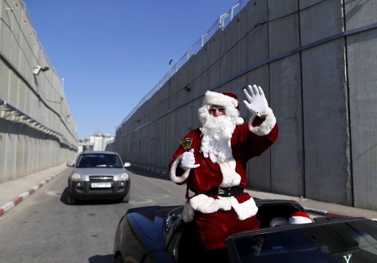 A man wears a Santa Claus costume as a convoy of cars transporting the Latin Patriarch of Jerusalem Fouad Twal crosses the Israeli barrier to celebrate Christmas in the West Bank city of Bethlehem December 24, 2015