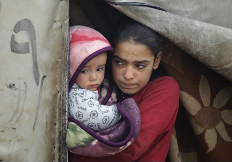 A girl carries her brother as she stands at the entrance of her tent during the cold weather in a camp for internally displaced people in Idlib province, Syria