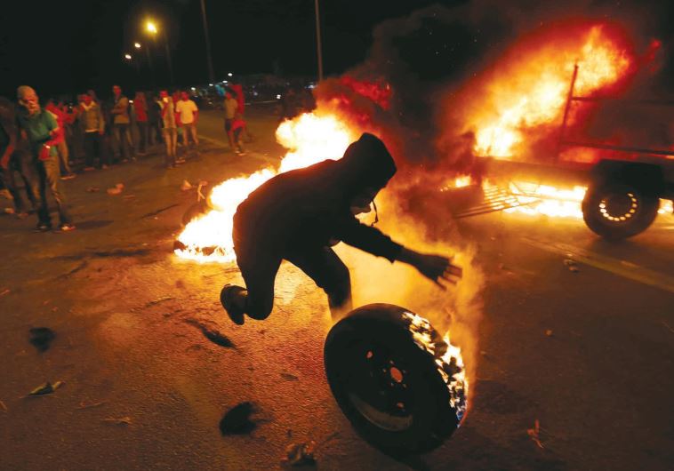 An Israeli Arab rolls a burning tire in a protest in the southern village of Hura in November 2013