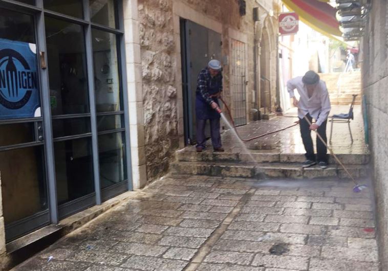 Raphael Kohn (right) washes the street outside his Nahalat Shiva restaurant this past week, together with a 90-year-old shoemaker who has had a store in the area for 35 years