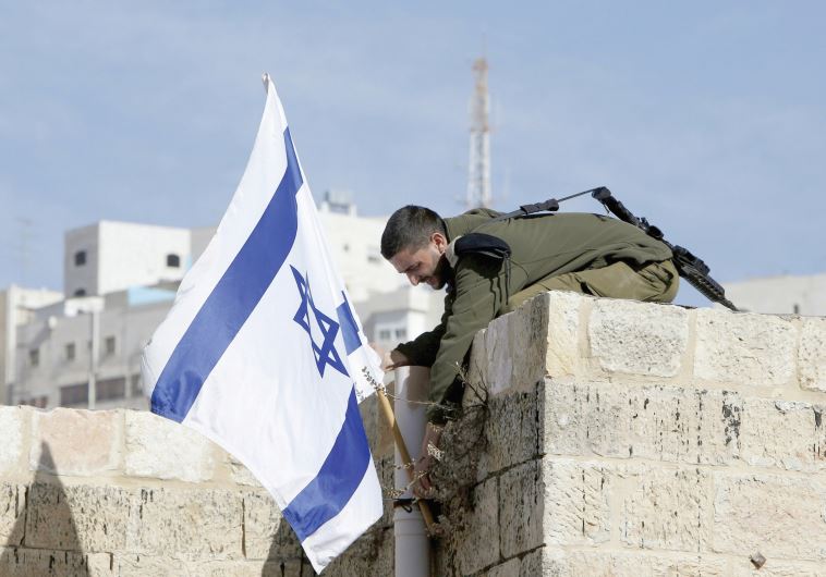 A SOLDIER holds a flag atop a house in Hebron.